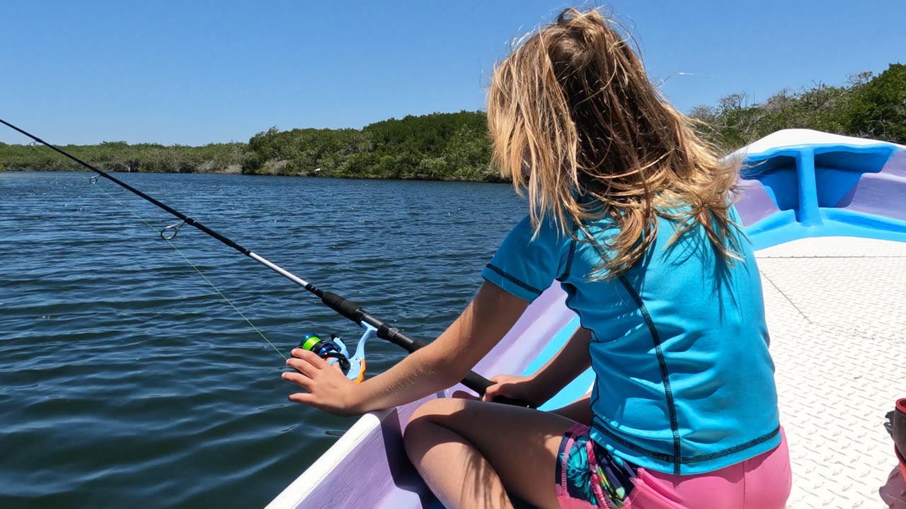 Girl holding a fishing reel while sitting in a small boat on calm water.