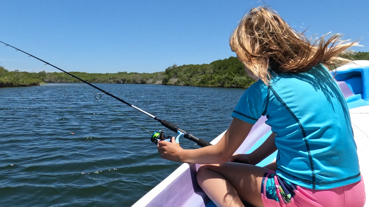 Girl holding a fishing rod as wind blows her hair on a boat.