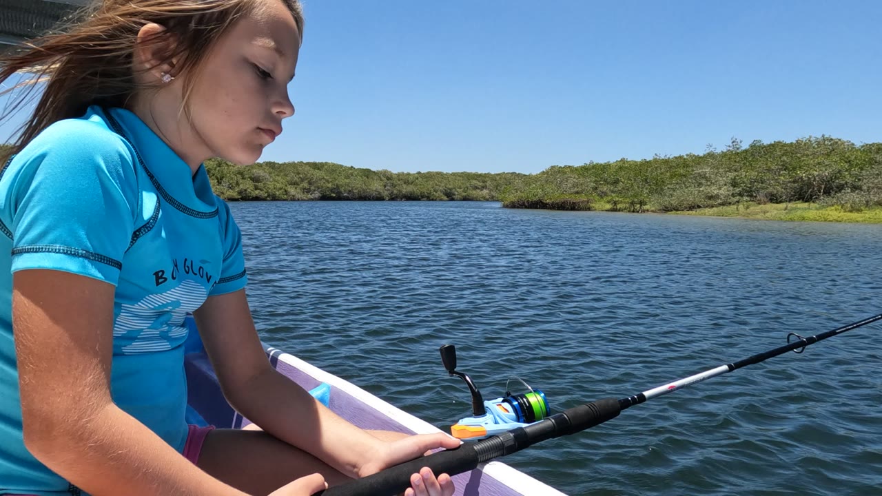 Girl looks down while holding a fishing rod in a small boat.