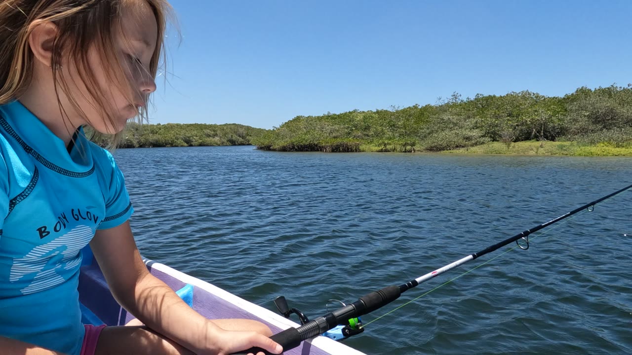 Girl seated in a boat holding a fishing rod over blue water.