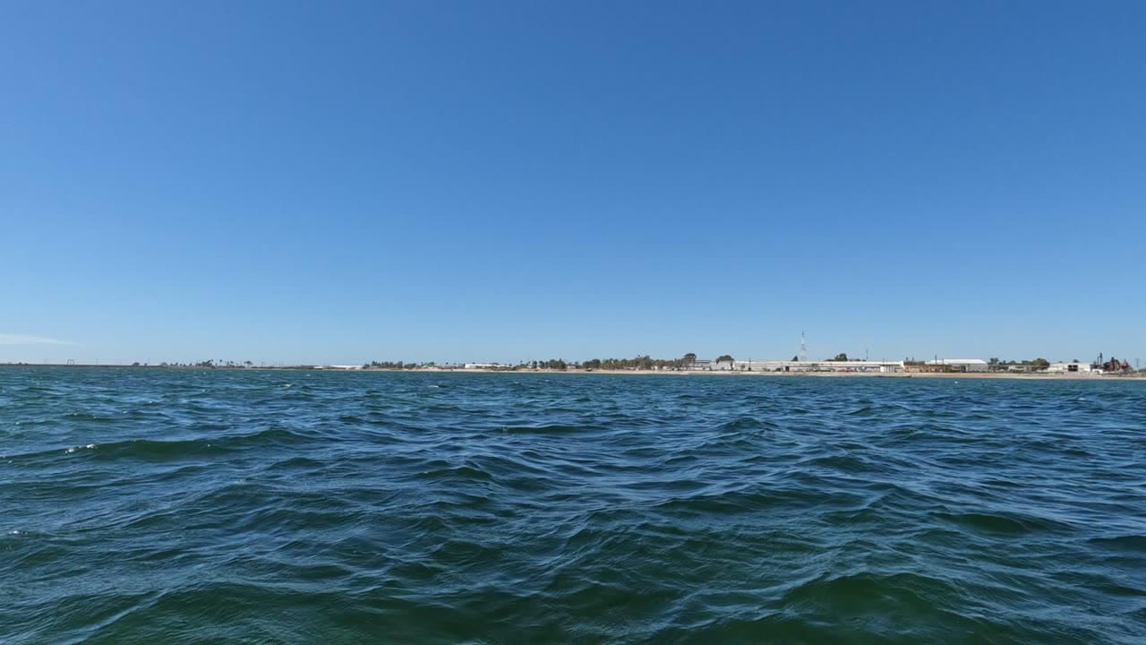 Blue-green waves with a flat distant shore and clear sky.