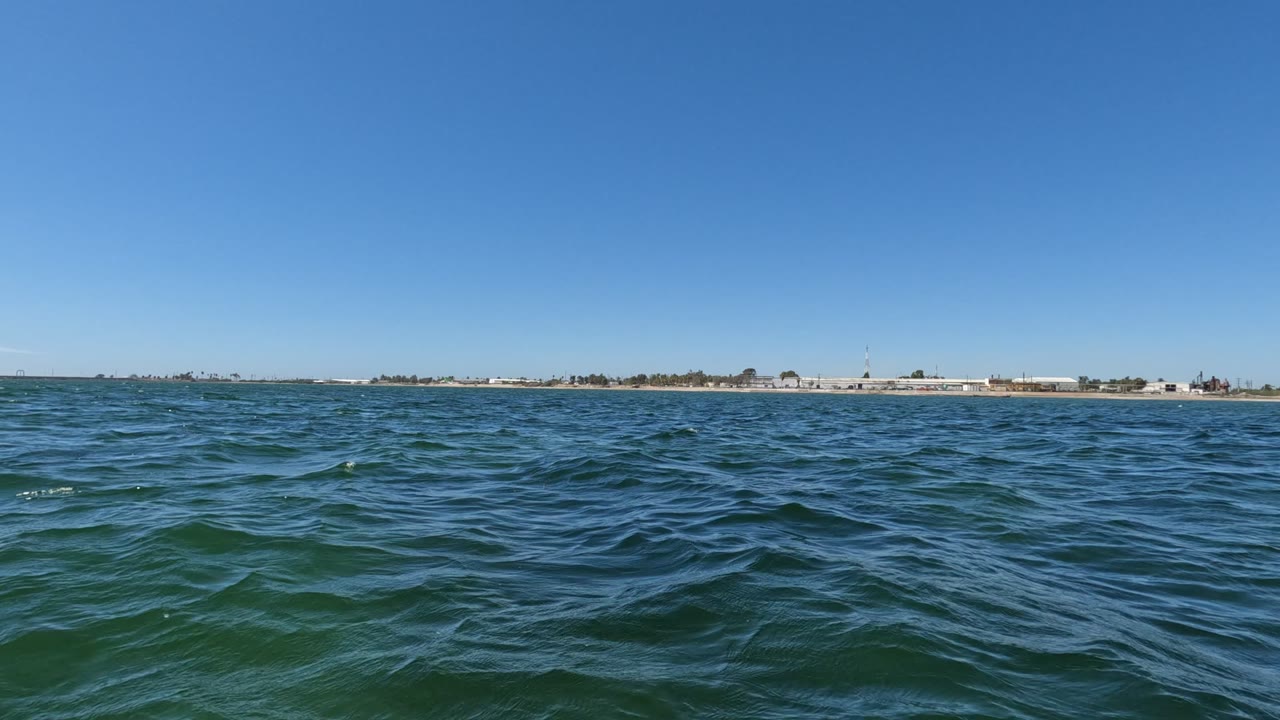 Low ocean surface with ripples and a distant coastal horizon.