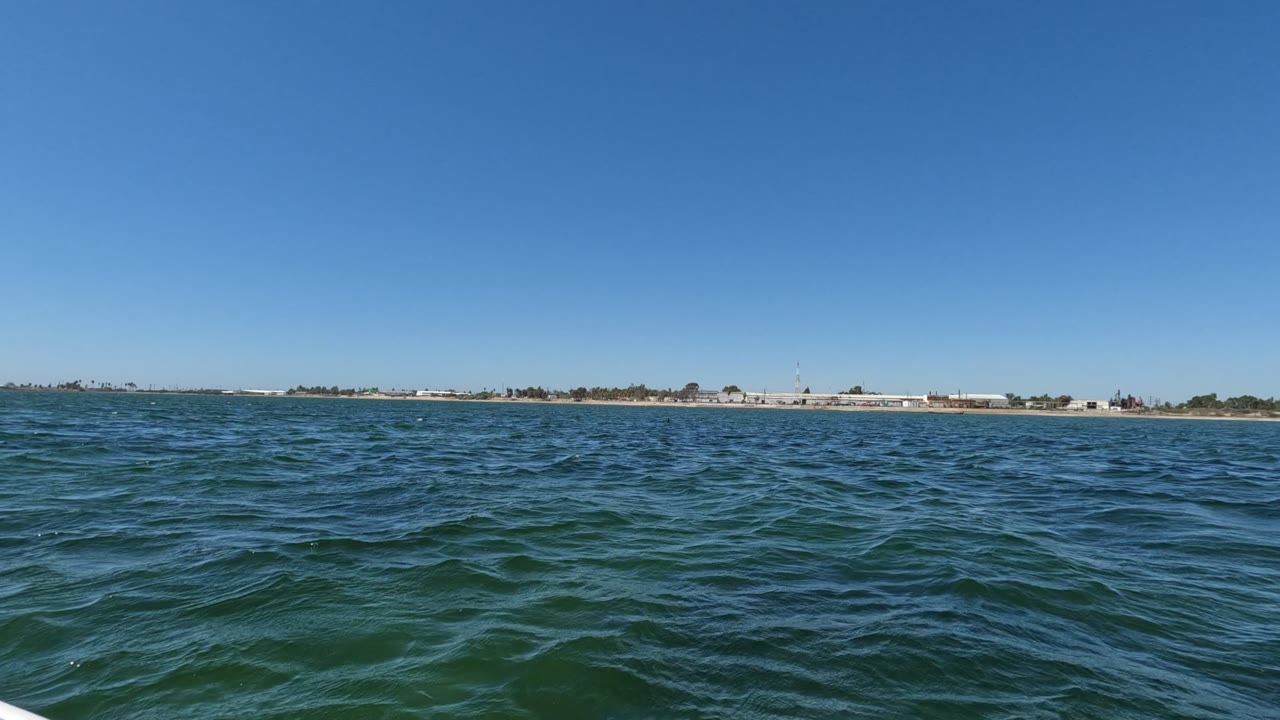 At two seconds, the frame holds mostly open Baja California water with the shoreline stretched thin across the horizon, clear blue sky above, and no visible people.