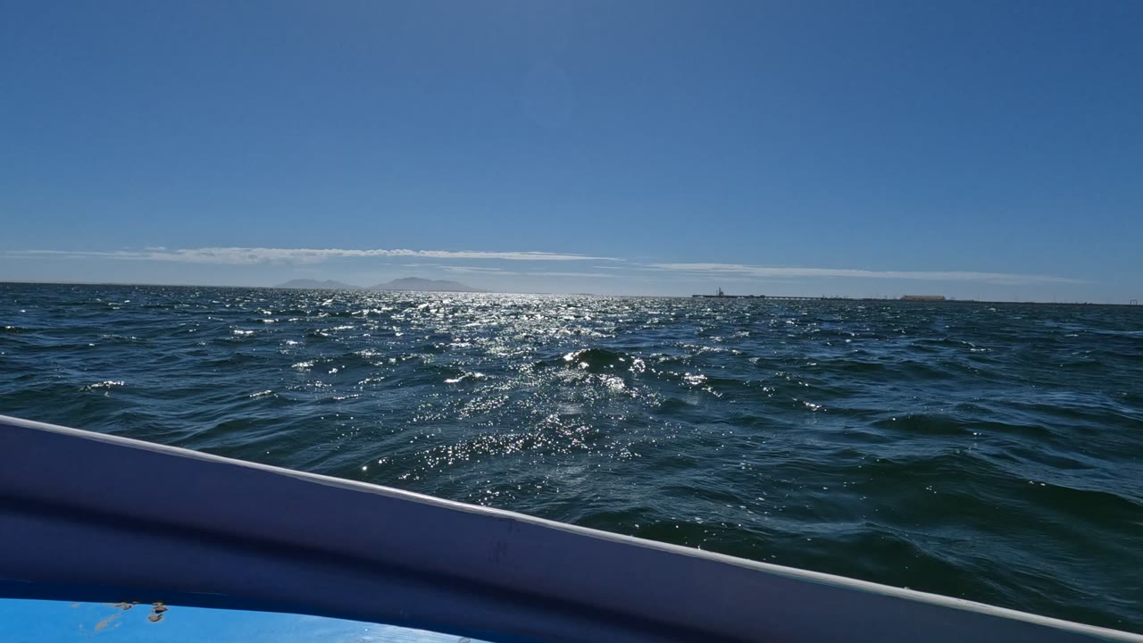 Opening frame from Baja California, Mexico showing a boat railing across the foreground, sparkling ocean water beyond it, a distant horizon, and no visible people.