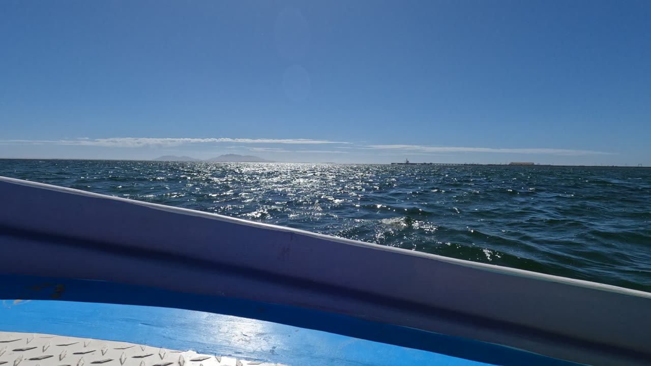 Open ocean with bright sun shimmer seen over a boat rail.
