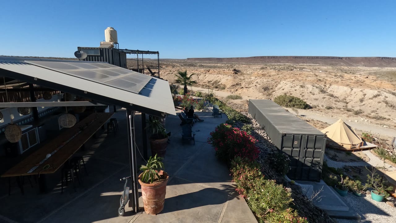 Outdoor patio with solar panels, plants, container, tent, and desert hills.