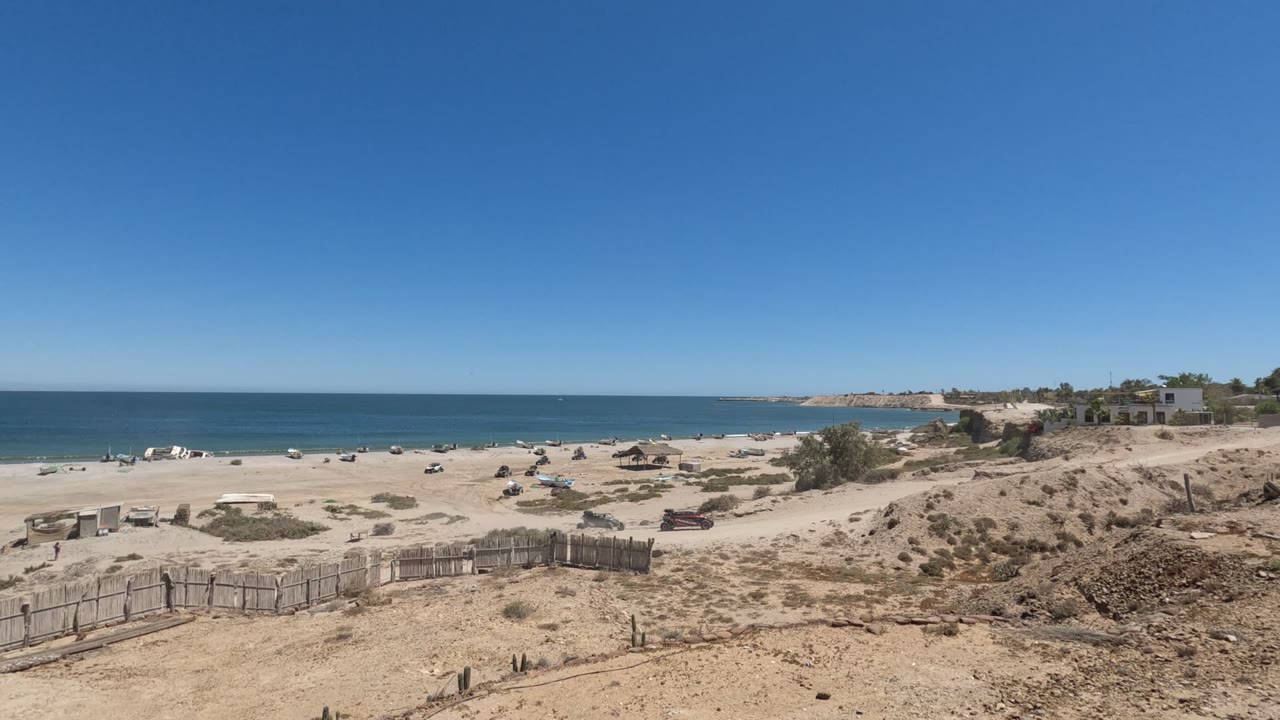 Sandy beach and dune foreground with calm ocean and distant buildings.