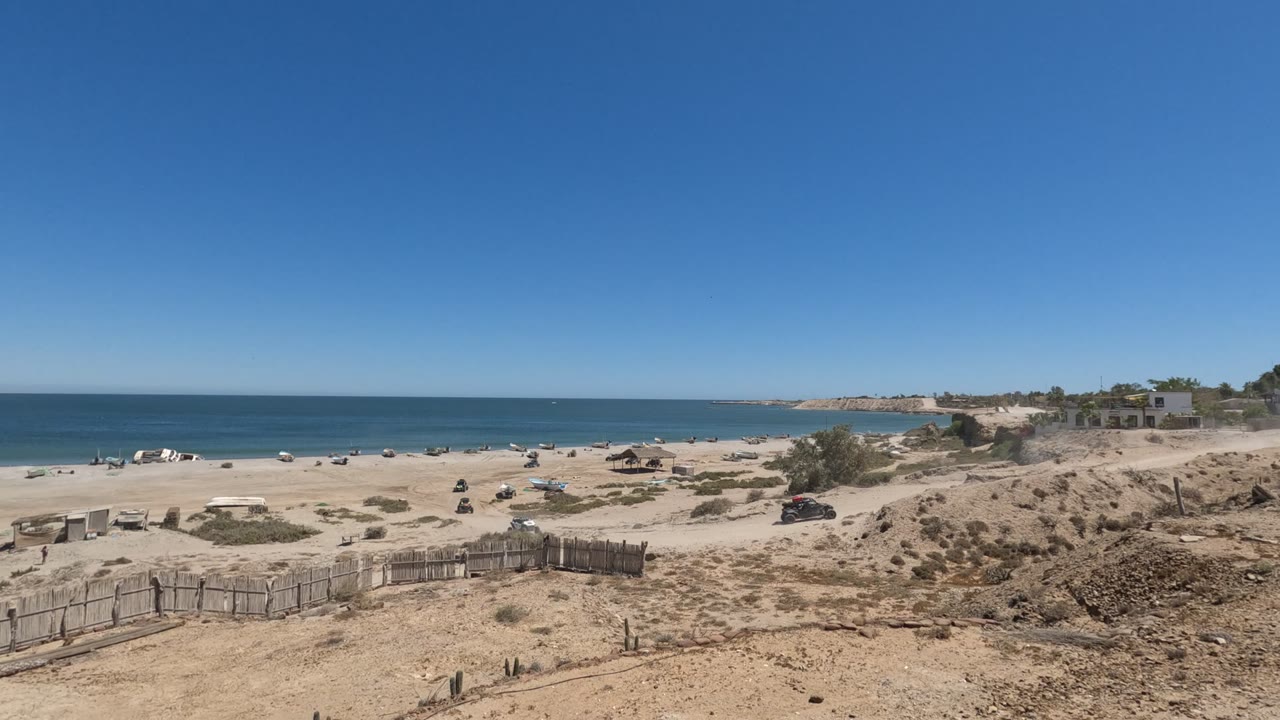 Sandy coastal road beside a beach with vehicles and ocean horizon.
