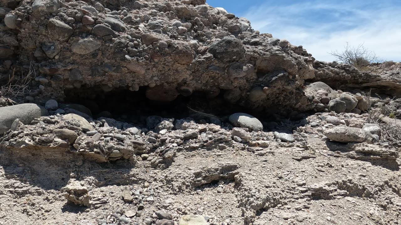 Dry stony ground below a rough rock overhang.