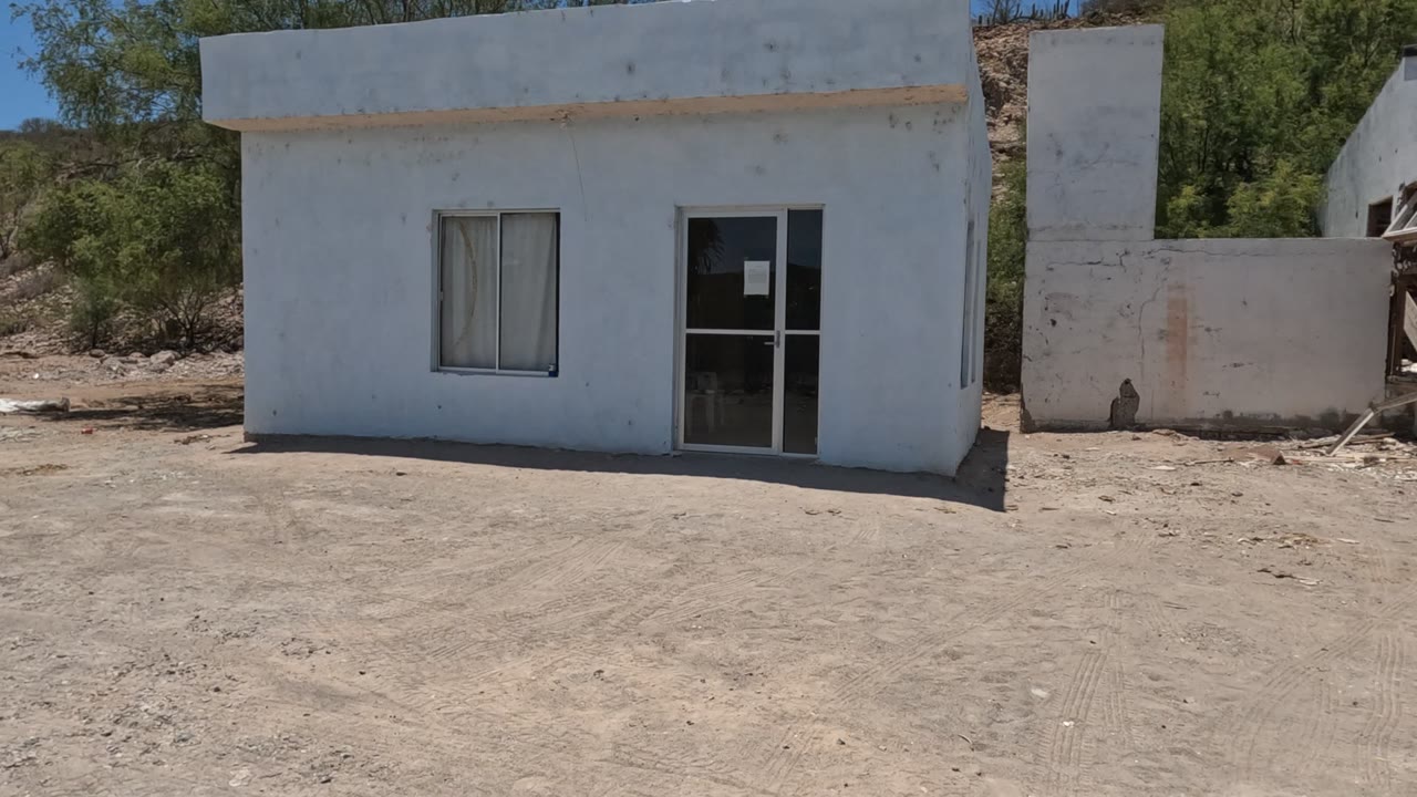 White structure and adjoining damaged wall beside rocky dirt ground.