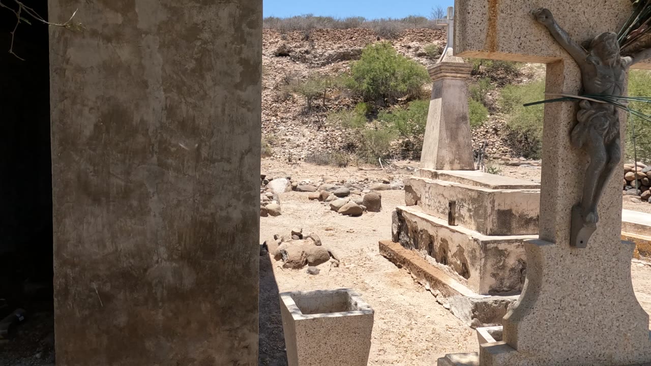 Crucifix and grave markers framed by a concrete cemetery structure