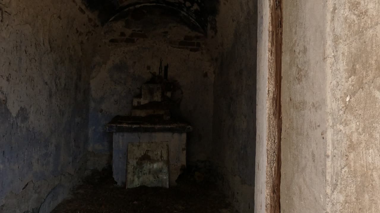 Inside a weathered abandoned structure in Baja California, Mexico, a small altar-like feature sits against rough stained walls with no visible people.