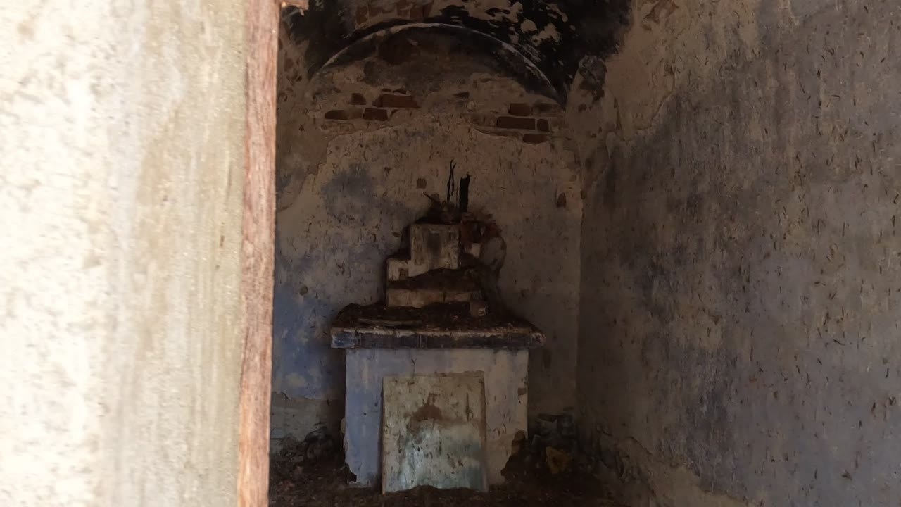 The interior ruin in Baja California, Mexico is partly blocked by a bright rough wall edge, with a small altar-like feature in the dark background and no visible people.