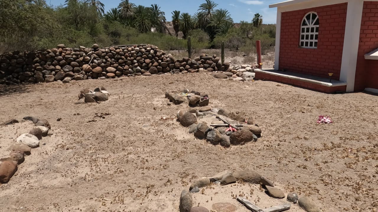 Stone graves in sandy ground with a red brick chapel at the right edge.