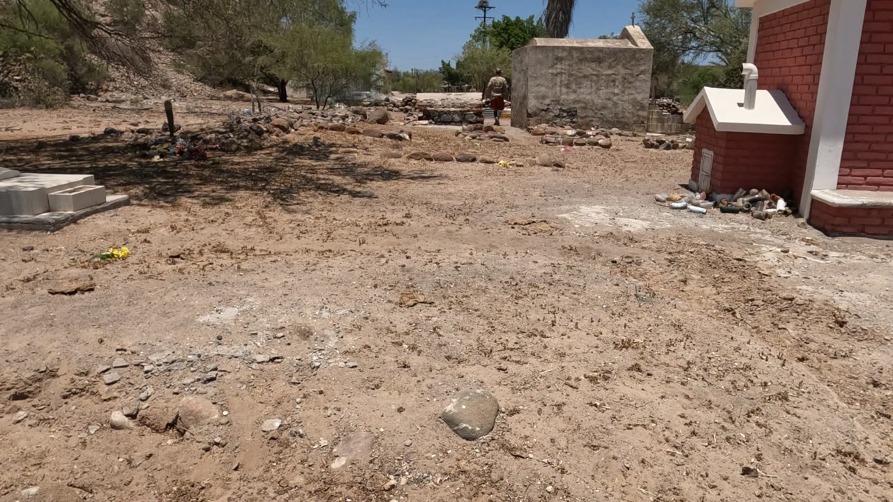 Dry cemetery landscape with red brick structure and scattered rocks.