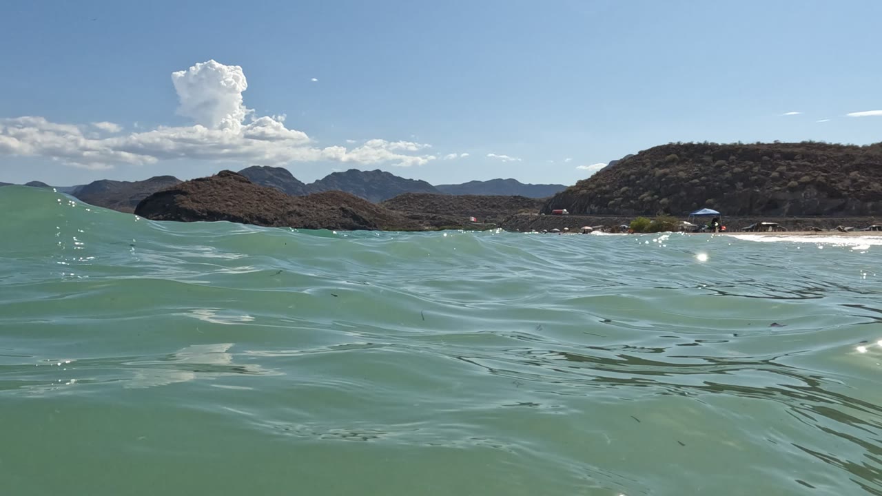 Rippling ocean surface with a sandy shoreline and dry hills under blue sky.