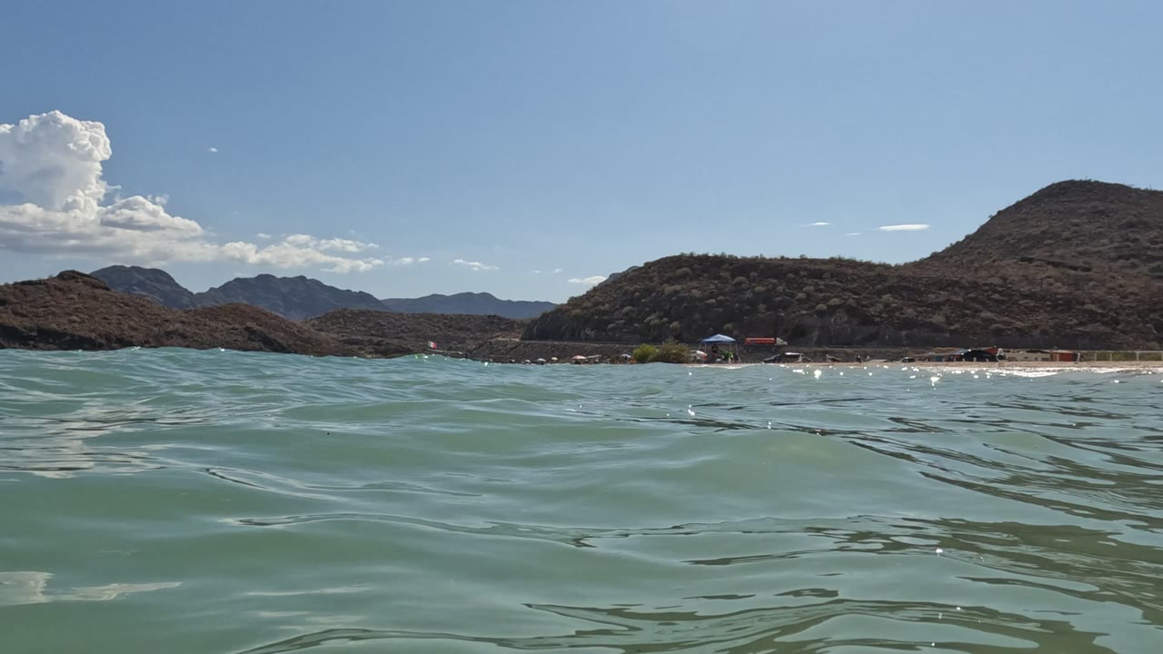 Small wave crest in front of distant beach and hills