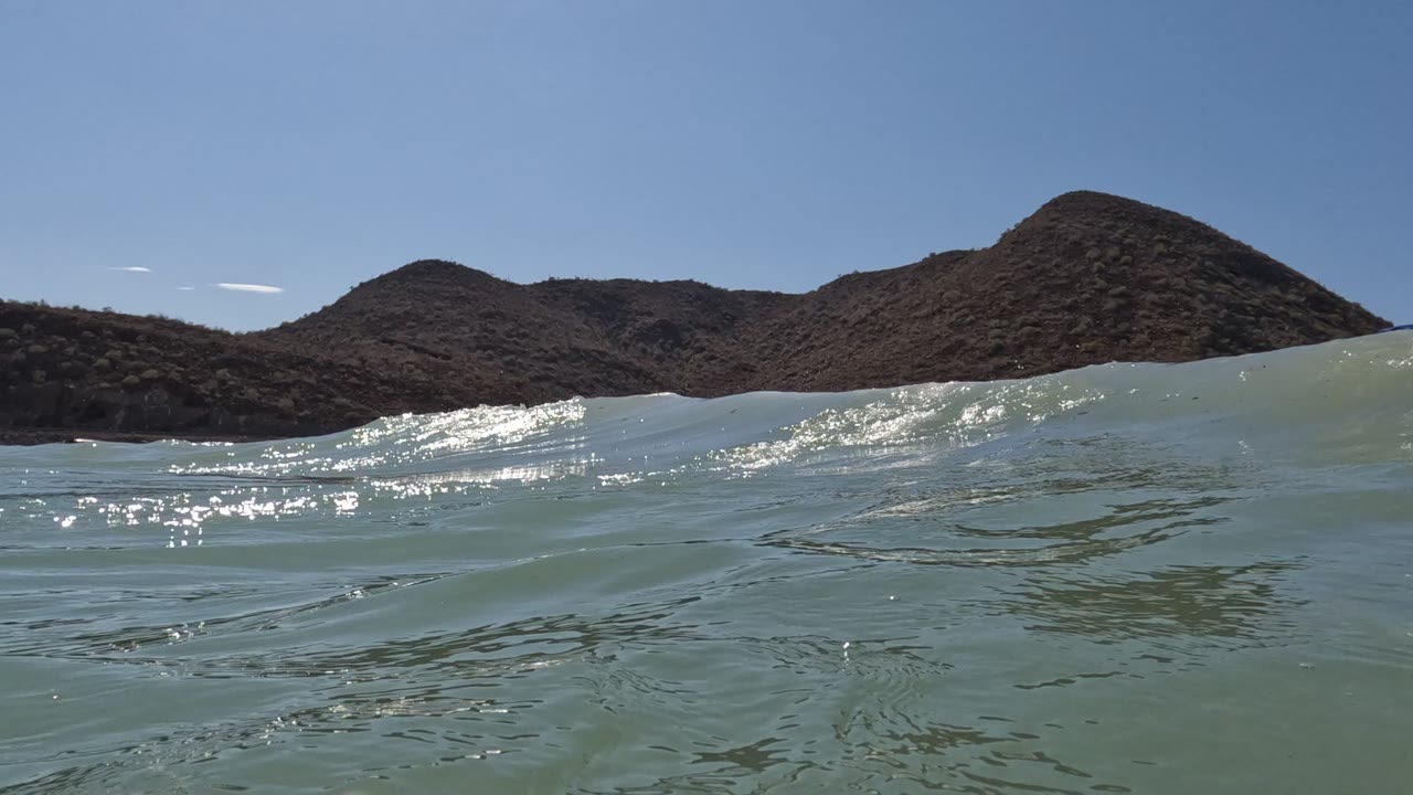 Waterline view of small waves with dry hills and clear sky beyond.