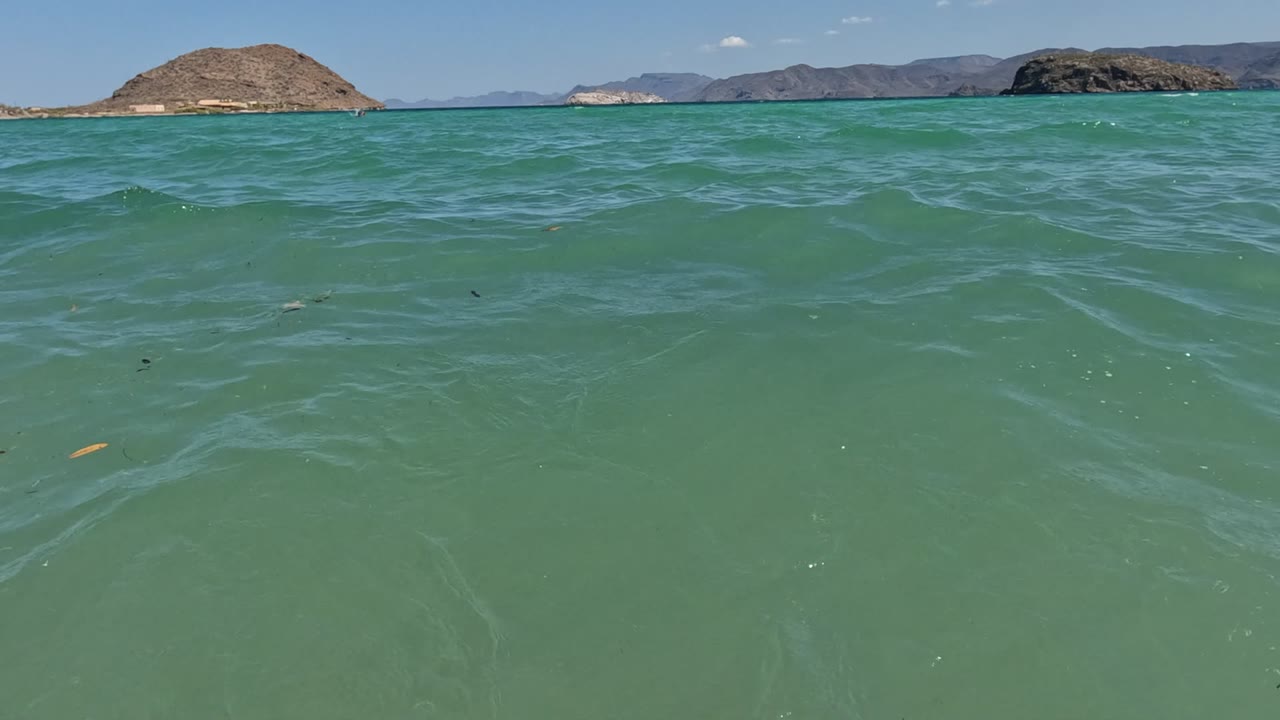 Water-level view of turquoise-green sea in Baja California, Mexico, with low rocky islands spread across the horizon and no visible people.