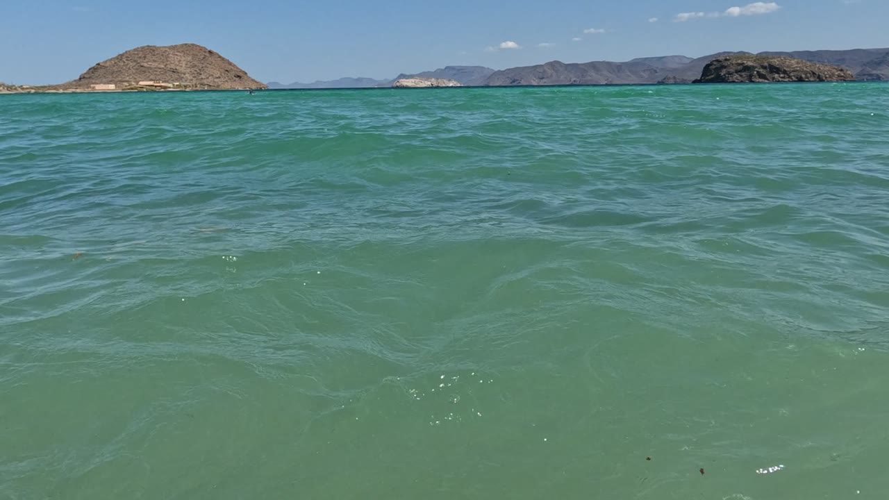 Small waves cross green-blue water with rocky islands in the distance.