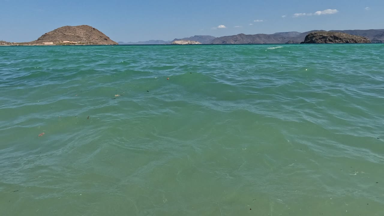 Open turquoise water fills most of the frame in Baja California, Mexico, with low rocky islands along the horizon and no visible people.