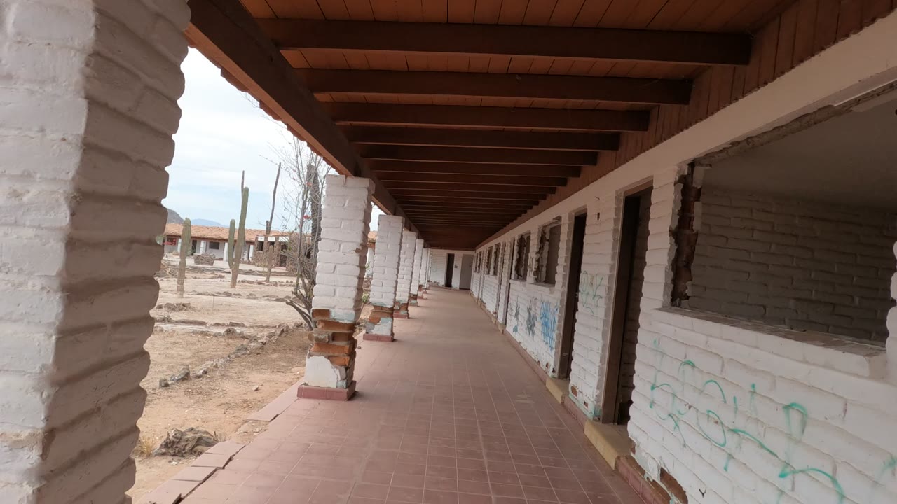 Long tiled corridor with white columns and desert outside