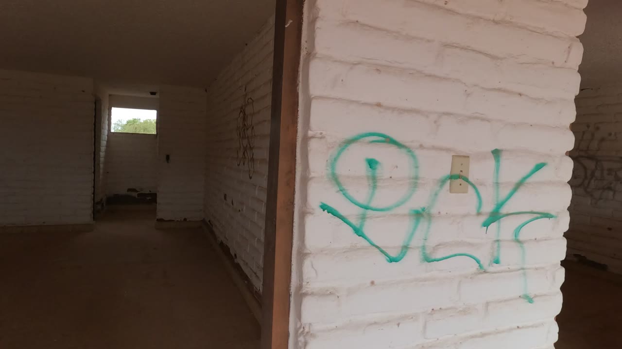 Start of the Baja California, Mexico clip showing a dim empty white brick corridor with green graffiti close to camera and no visible people.