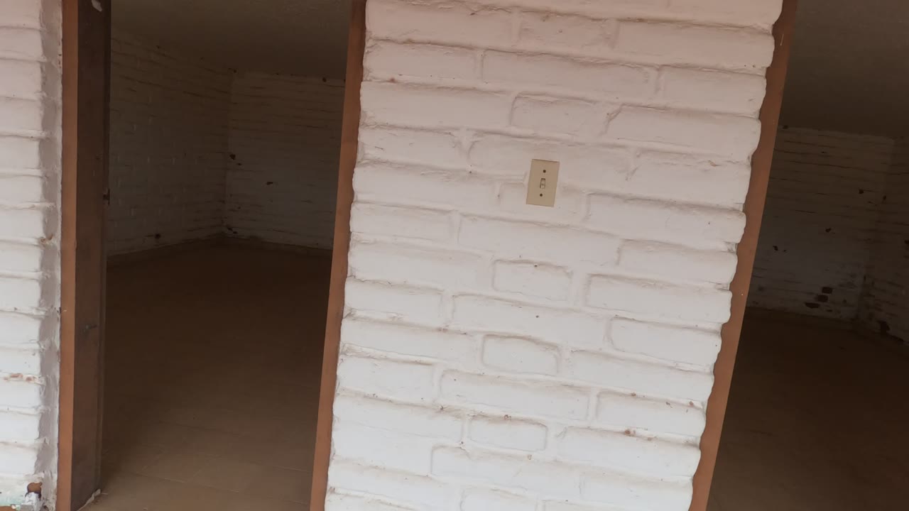 A white brick column and rough doorway edge frame a dark empty room in Baja California, with a small rear window and no visible people.