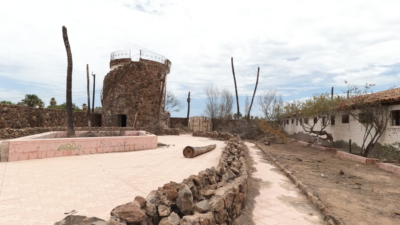 Stone tower courtyard with a log on pale paving and a low rock wall.