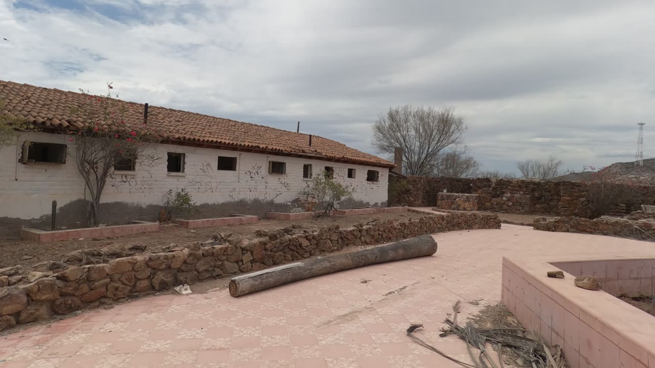 Stone courtyard and white rural building under cloudy sky.