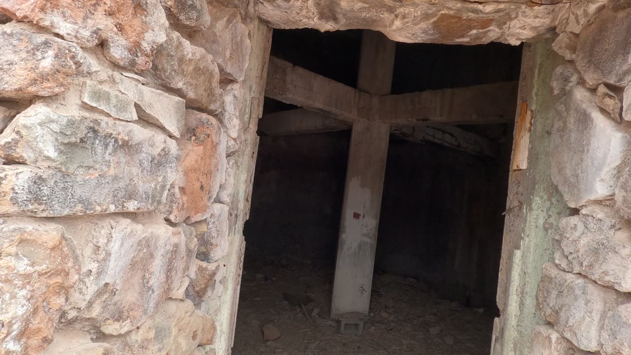 Close view from a rough stone doorway into a dark abandoned room in Baja California, Mexico, with concrete supports inside and no visible people.