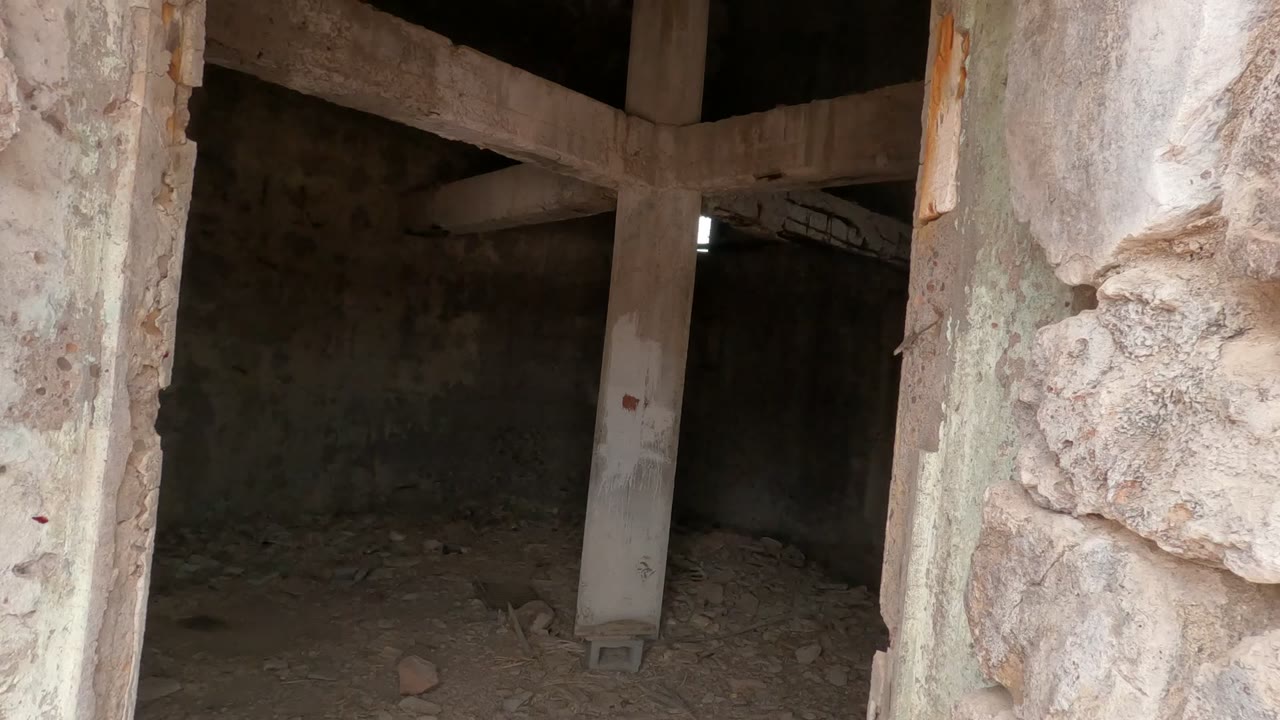 A rough stone edge and damaged plaster frame a deeper view of the abandoned room in Baja California, Mexico, with stained walls and no visible people.