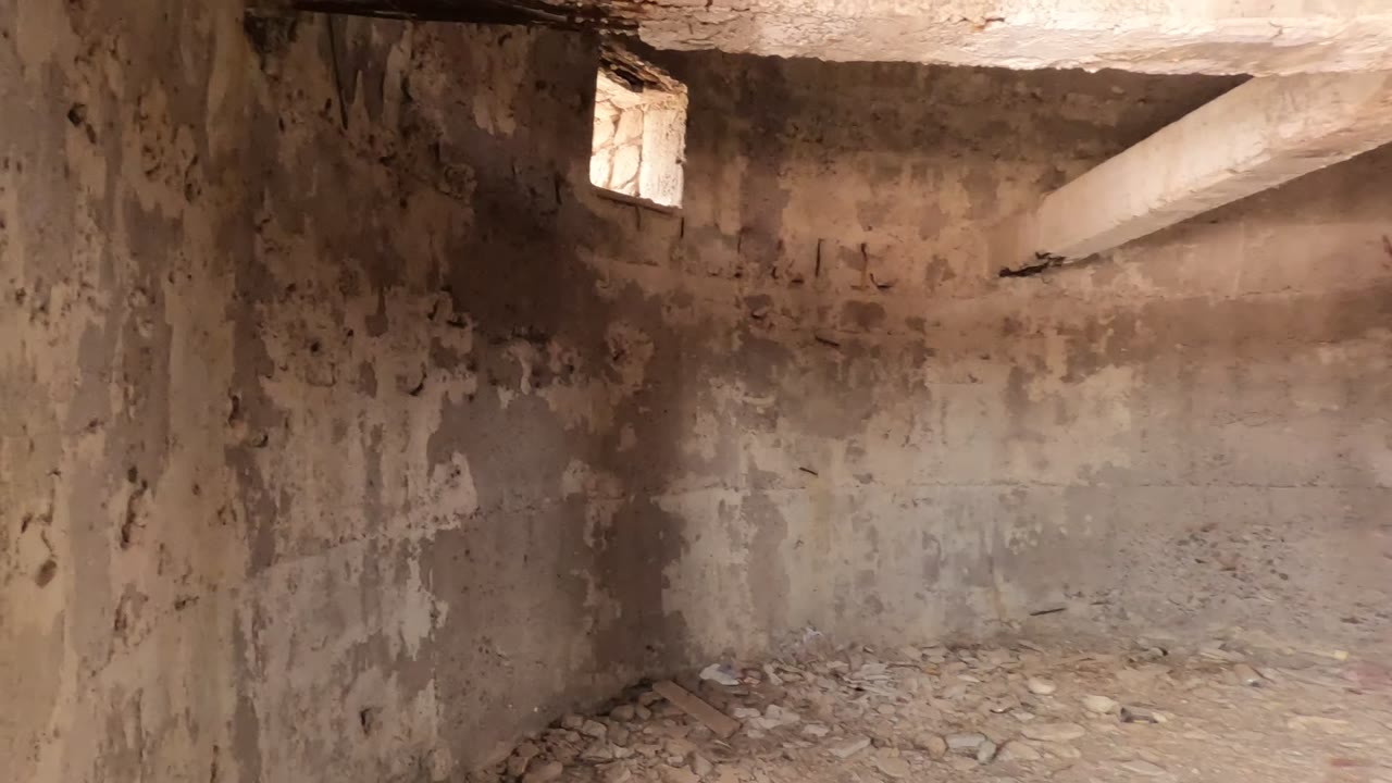 Wide interior view of an abandoned concrete structure in Baja California, Mexico, showing stained walls, floor debris, a small window, and no visible people.