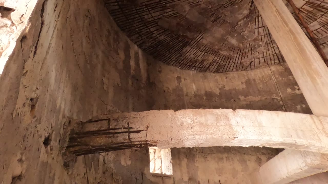 Upward interior view in Baja California, Mexico, showing a rough concrete column rising toward a circular wire mesh dome ceiling with no visible people.