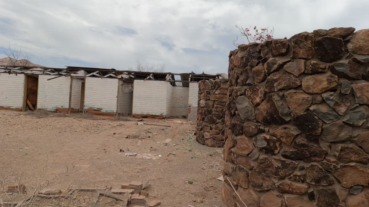 Weathered stone wall and white brick buildings across an arid courtyard.