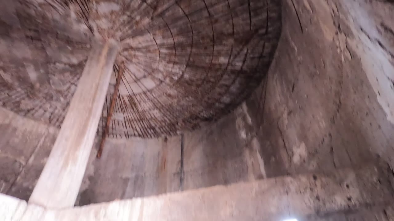 Early frame inside an abandoned concrete structure in Baja California, Mexico, looking up at a damaged domed ceiling with exposed rebar, stained walls, and no visible people.