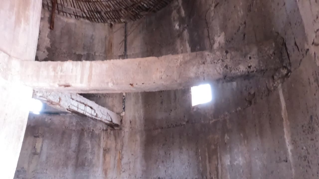 Interior view in Baja California, Mexico showing a curved concrete ceiling, a bright rectangular wall opening, rough stained walls, and no visible people.