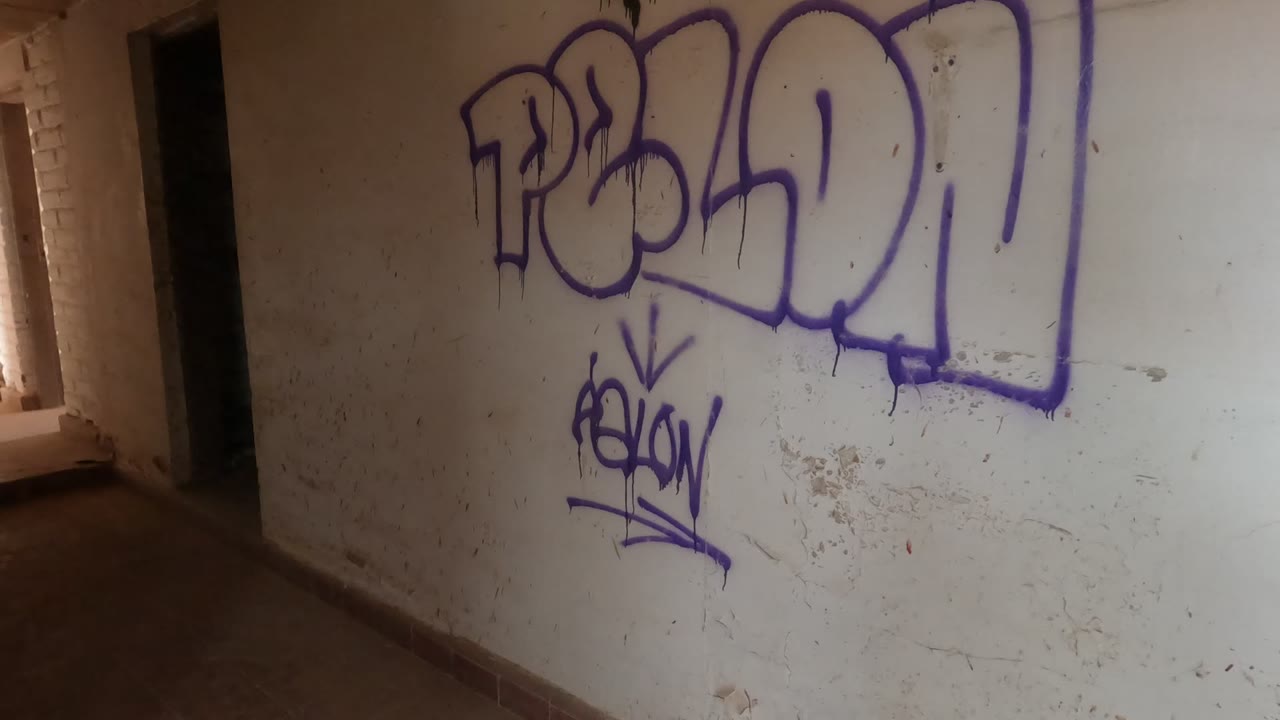 Purple graffiti fills a white wall inside an abandoned building in Baja California, Mexico, with a dark doorway on the left and no visible people.