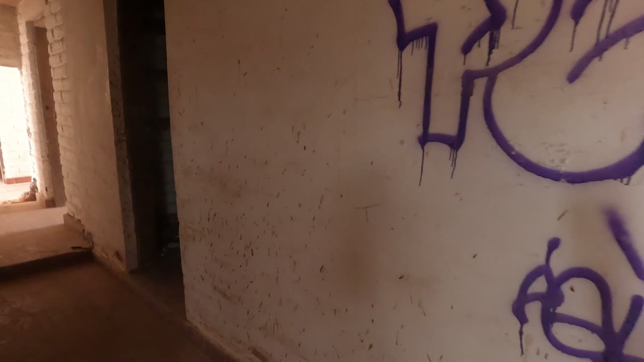 A closer portion of the purple graffiti and lower tag sits on a marked white wall, with no visible people in this Baja California, Mexico interior.