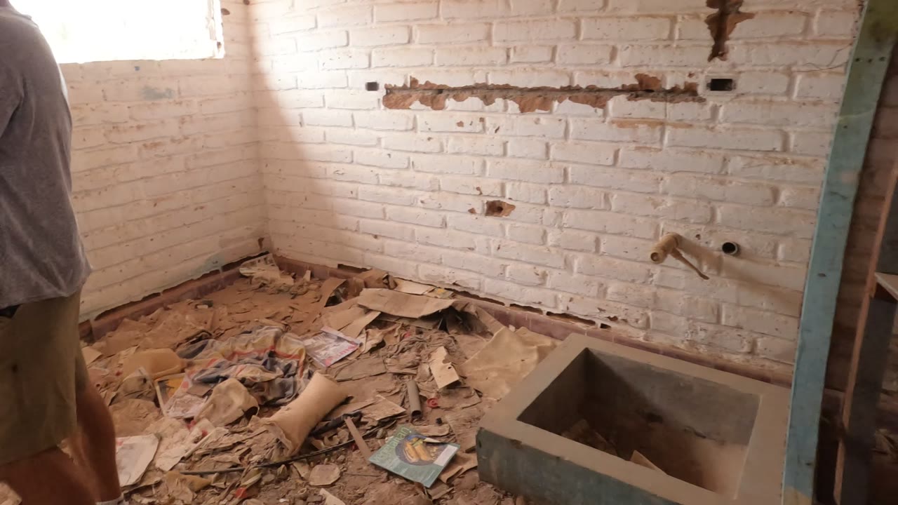 Baja California, Mexico room corner with bright window light on white brick, loose debris across the floor, and a concrete sink in the foreground with no visible people.