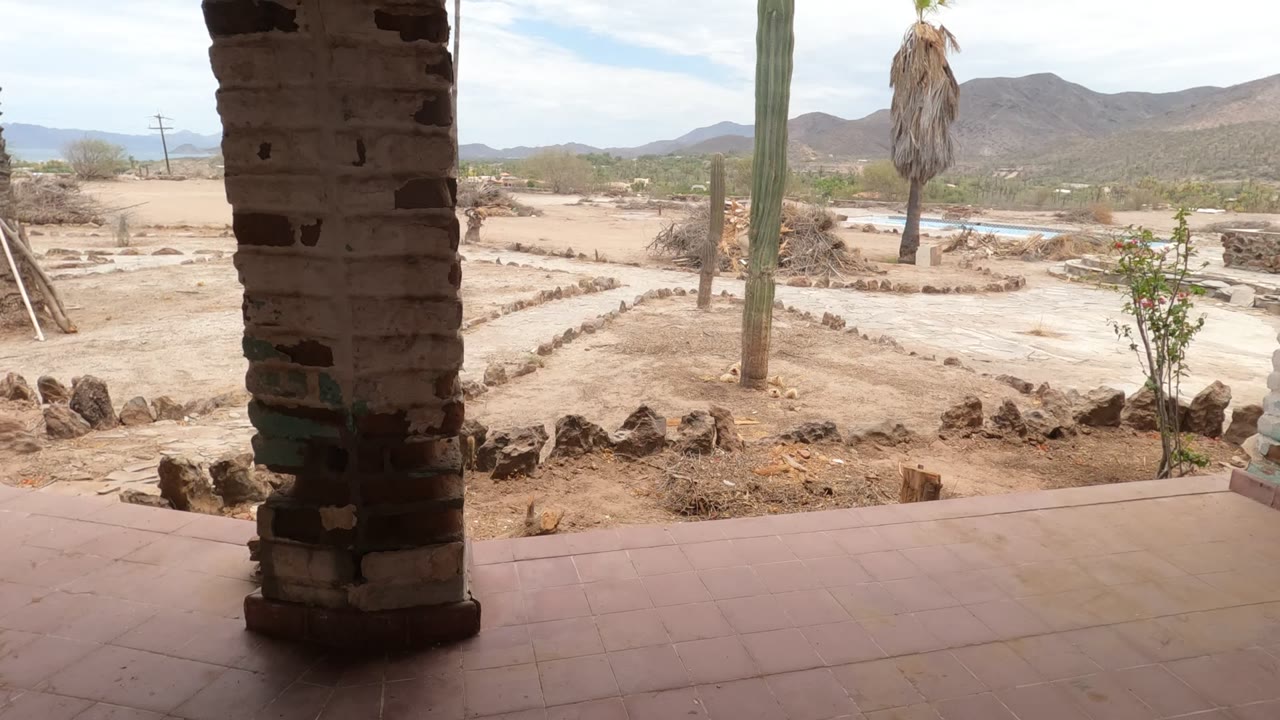 Patio column framing rock-bordered sandy paths and tall cacti