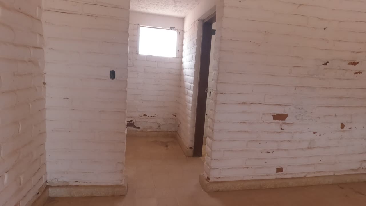 White painted brick room in Baja California, Mexico, with a small bright window, chipped wall patches, a doorway at right, and no visible people.