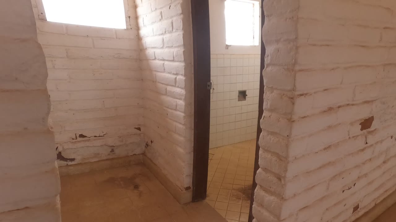 The view shifts along a white brick partition in Baja California, Mexico, toward a doorway where tiled wall surfaces start to appear, with no visible people.