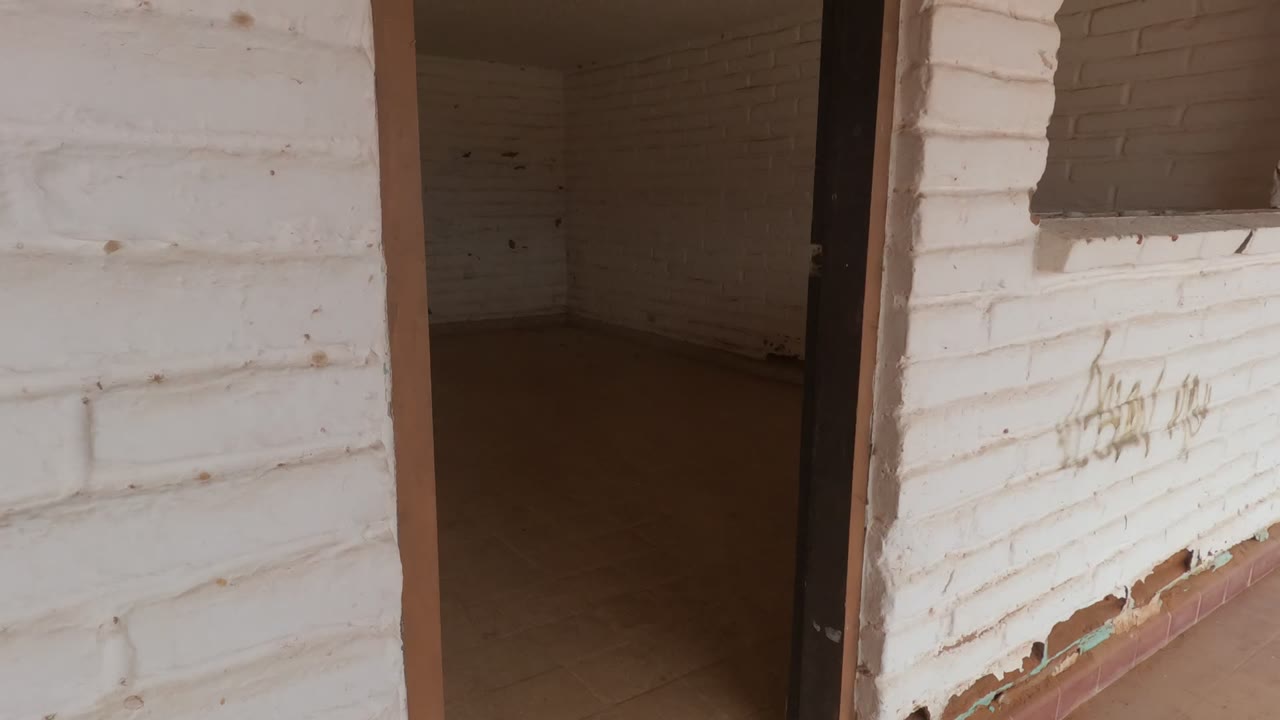 Doorway view into an empty white brick room in Baja California, Mexico, with worn paint on the foreground wall and no visible people.
