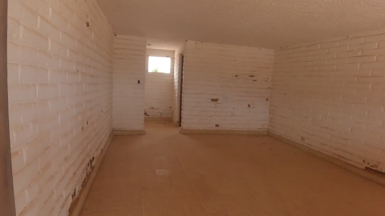 Long view across the empty white brick interior in Baja California, Mexico, with scuffed paint along the walls and a bright window in back, no visible people.