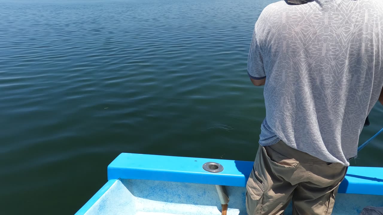 Man standing on a small blue boat facing open water.