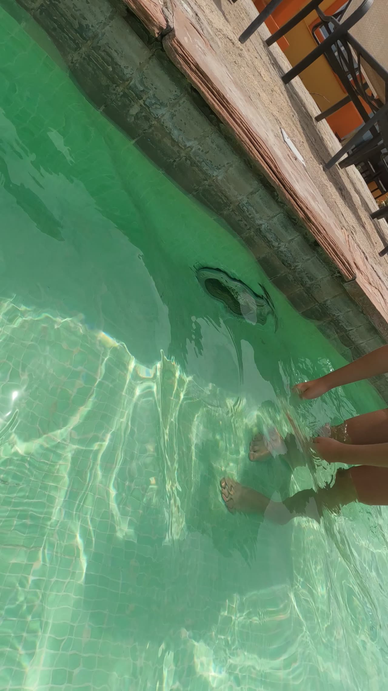 At 0:00 in Baja California, Mexico, the frame shows a child's lower body and arm partly underwater in a clear green-blue swimming pool beside a stone pool edge.