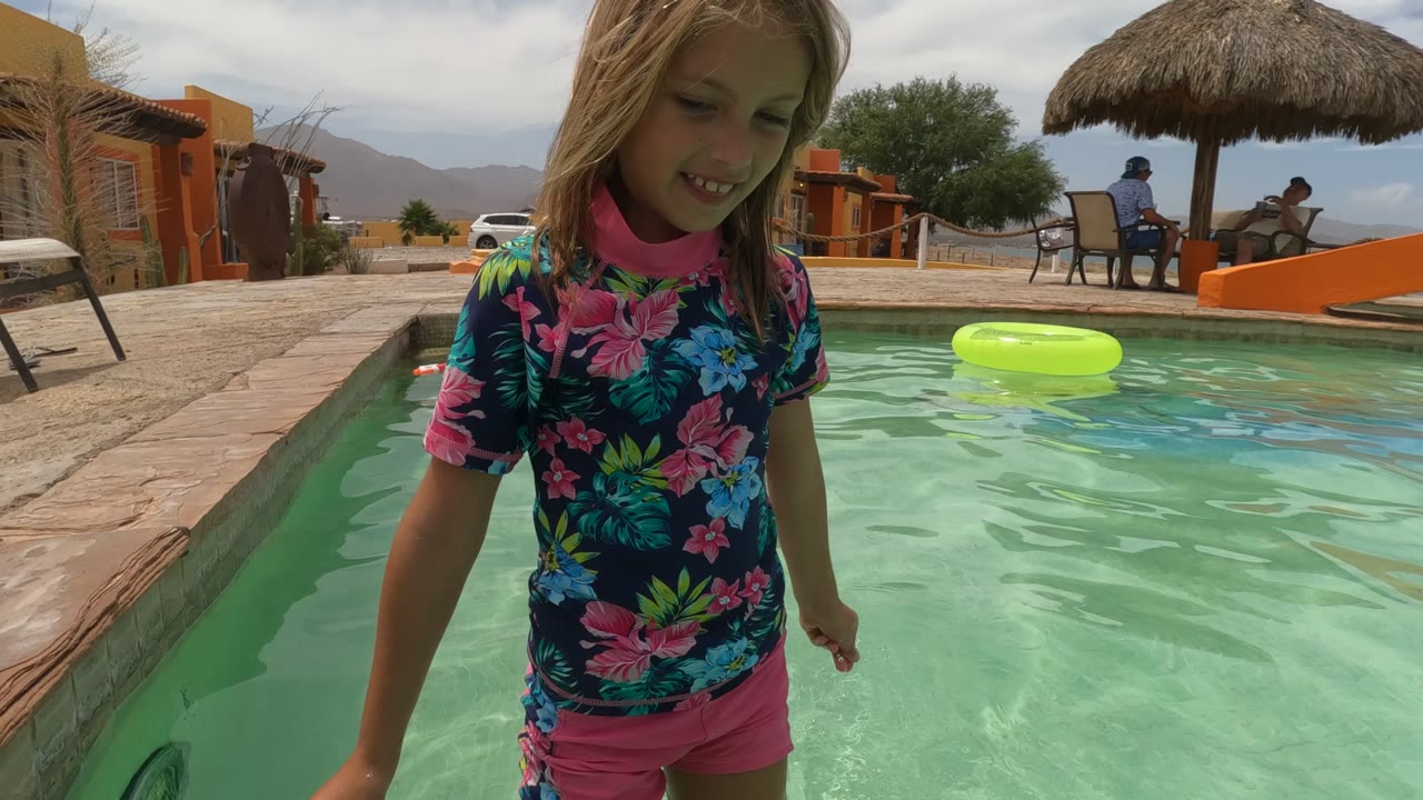 Child wading in pool beside the pool wall and green float.