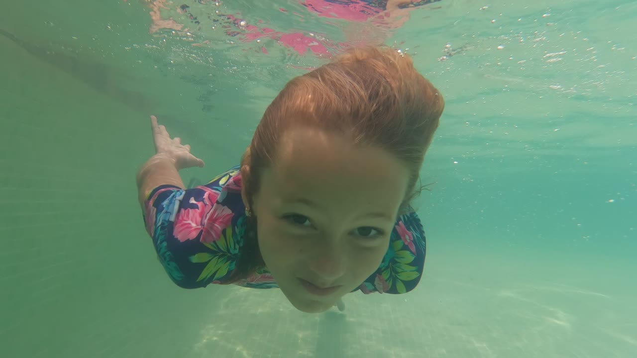 Child underwater facing the camera in a floral swimsuit.