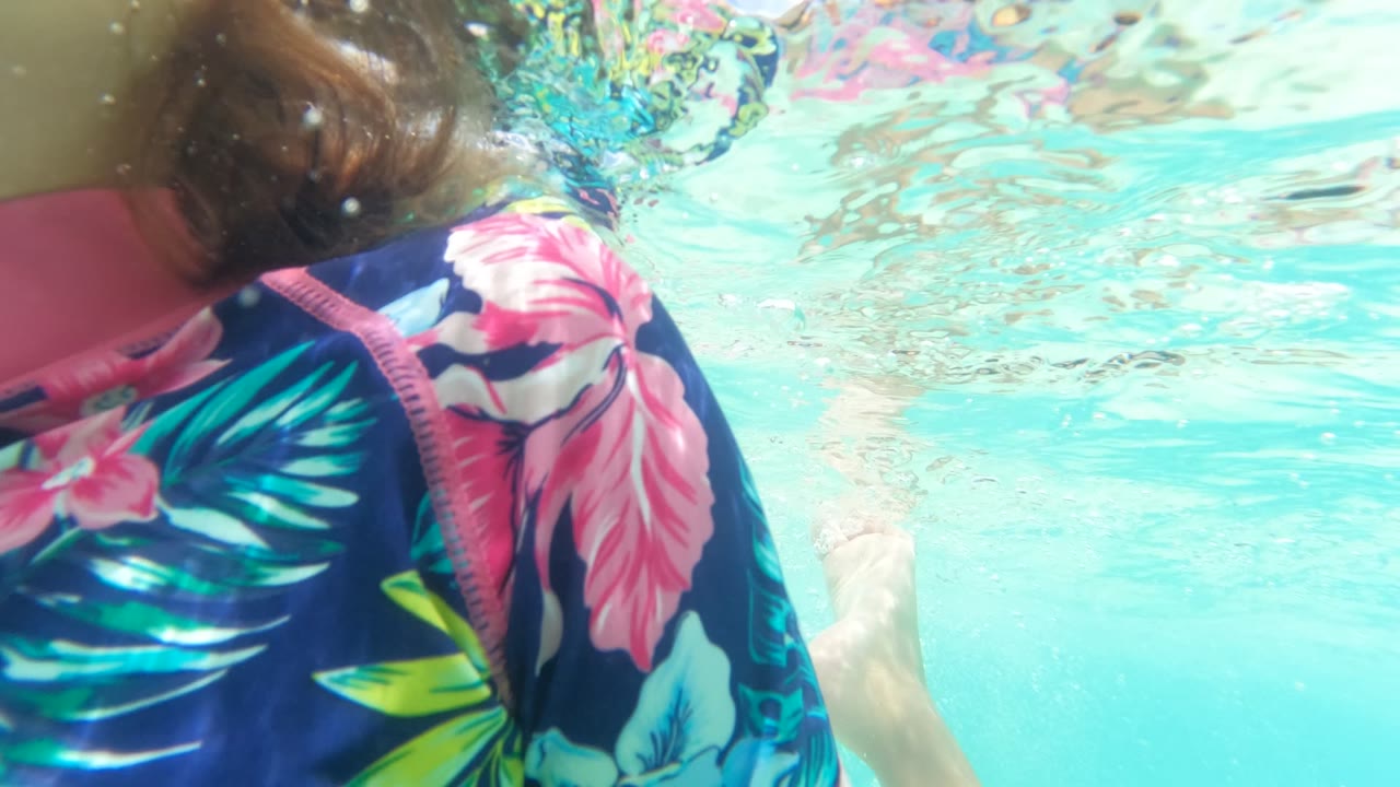 Child swimming underwater with an arm and leg visible in the pool.